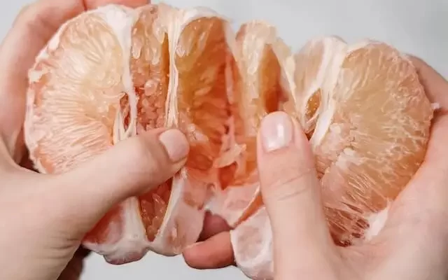A close up of raw pomelo flesh in the hands of a person.