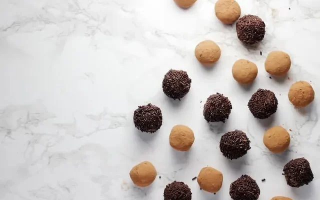 18 Truffle chocolates are spread on a white patterend background giving savoury vibes.